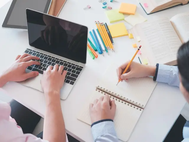 Dua orang menulis di buku catatan dan mengetik di laptop