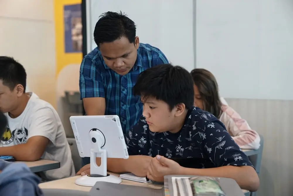 Pengajar membimbing siswa SMP yang menulis dengan tablet di kelas